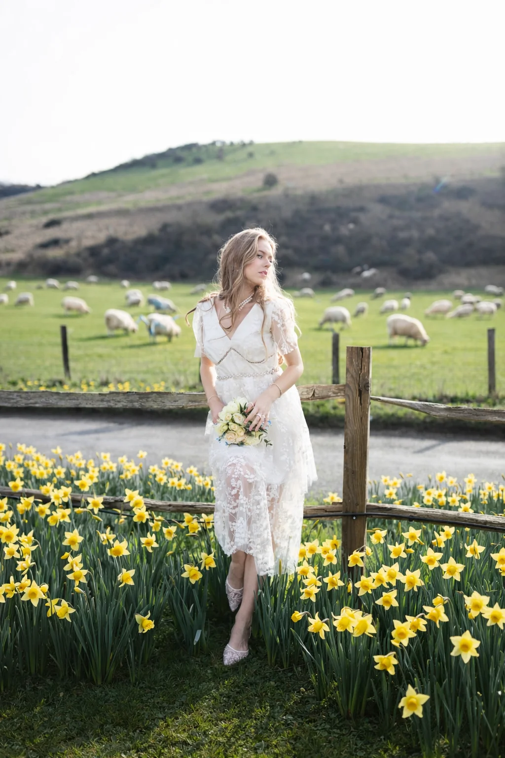 Bride holding a bouquet among daffodils, with sheep grazing on the hillside — Brighton countryside
